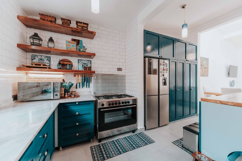 Stylish kitchen featuring sleek blue cabinets, stainless steel appliances, and wooden shelves.