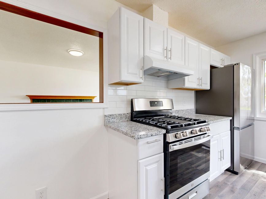Bright white kitchen featuring stainless steel stove and fridge with granite countertops.
