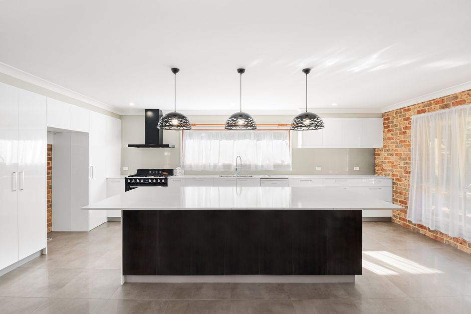 Spacious minimalist kitchen featuring white cabinets, pendant lighting, and brick walls.