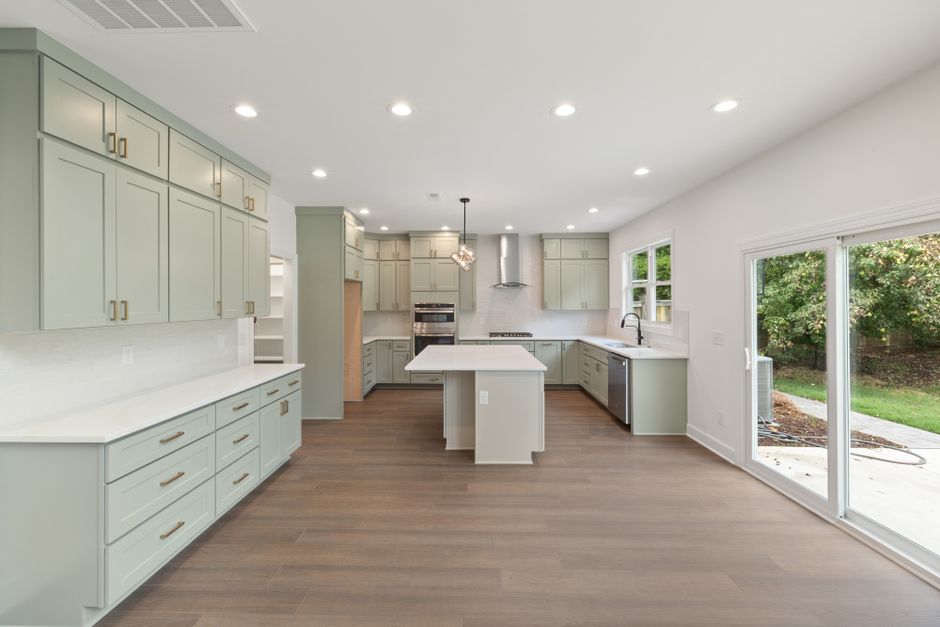 Spacious modern kitchen featuring an island, light green cabinets, and natural light from patio doors.