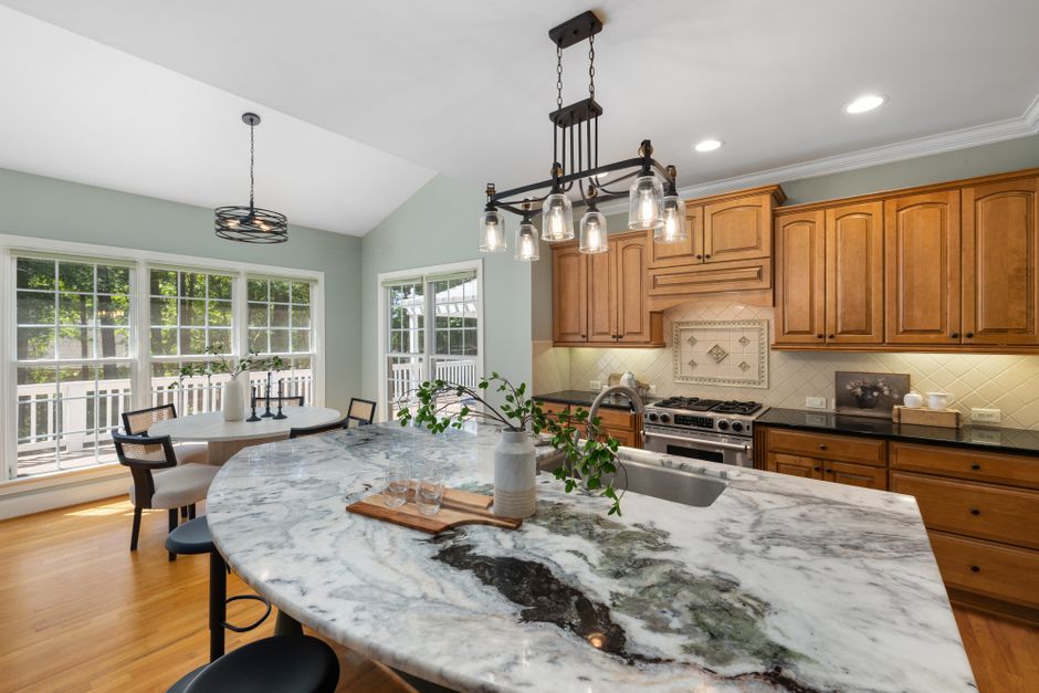 Bright and inviting kitchen interior featuring marble countertops, wooden cabinets, and large windows.